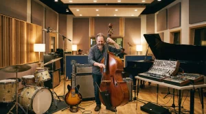 Contrabajista en estudio de grabación rodeado de diversos instrumentos